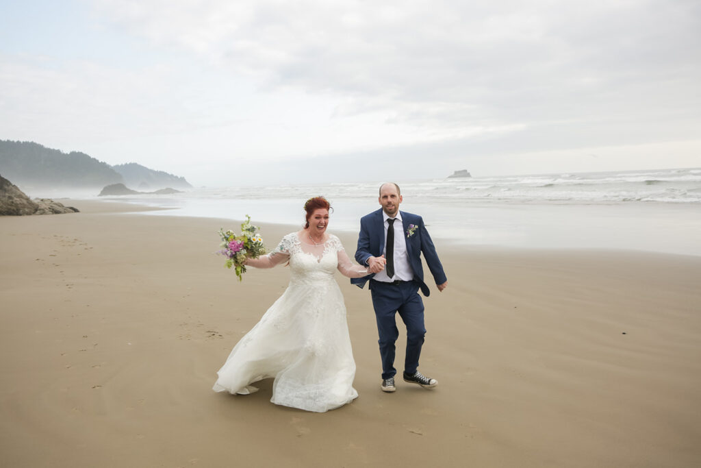excited bride and groom running along the oregon coast