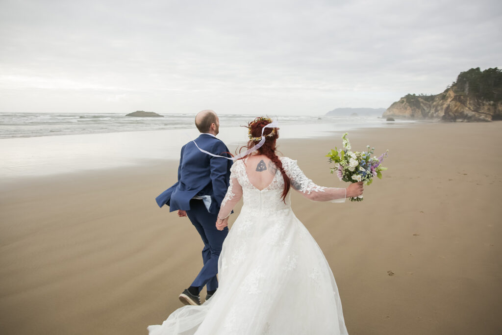 excited bride and groom running along the oregon coast