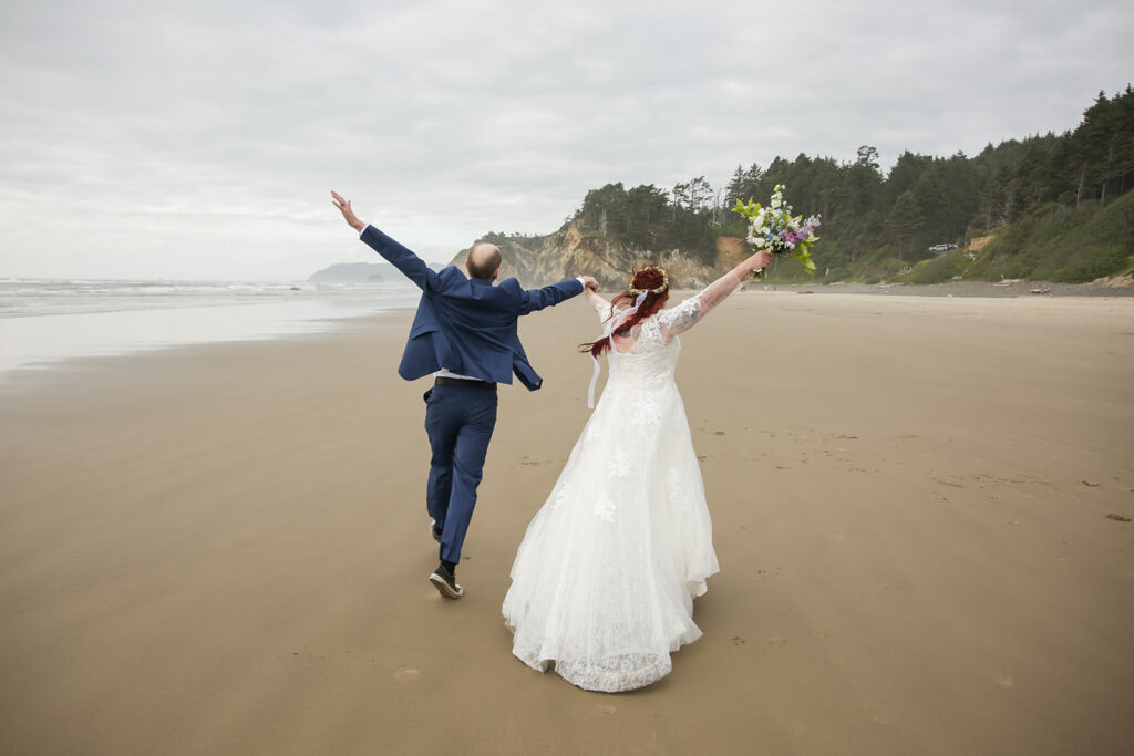 excited bride and groom running along the oregon coast